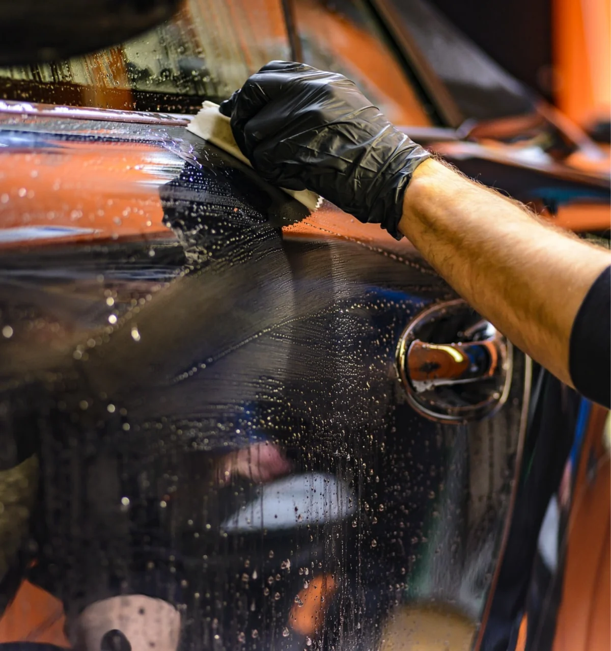 Profissional lavando veículo em ambiente de limpeza automotiva.